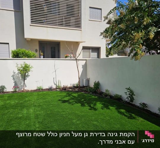 גינה עם דשא ירוק, עצים ושתילים לאורך הקיר